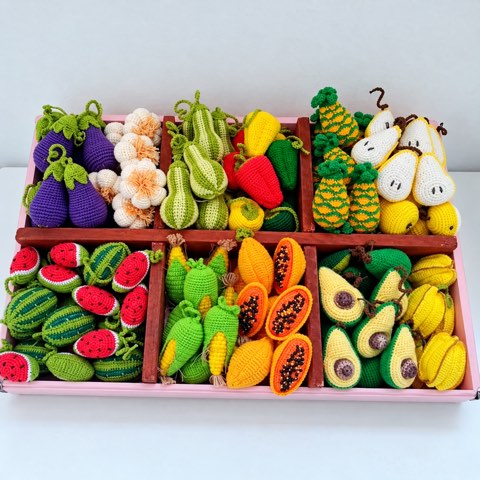 A divided tray holding dozens of mini crochet fruit and vegetables