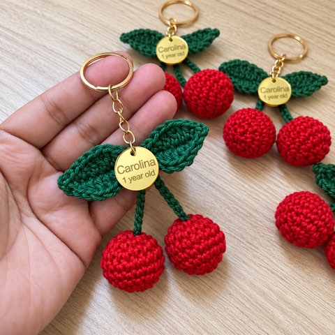 A hand holding crochet cherry keyrings with engraved tags