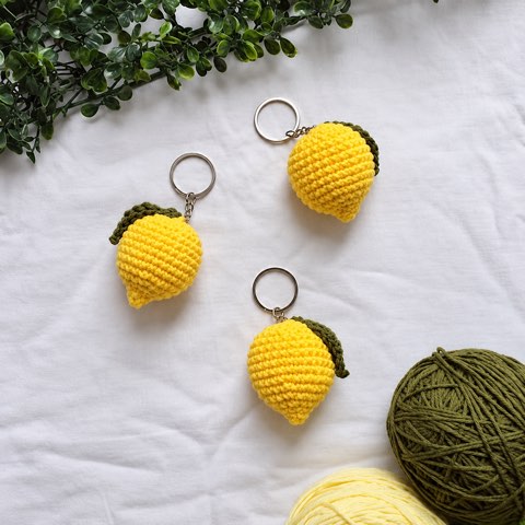 Small crochet fruit keyrings laid out beside a ball of yarn
