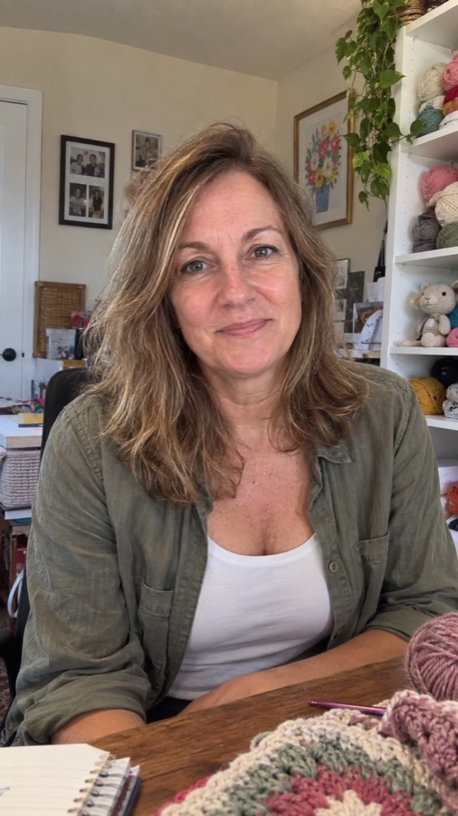 Laura Bennett in her craft room, shelves of yarn and a finished crochet piece behind her