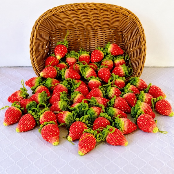 A basket tipped over with dozens of crochet strawberries spilling out