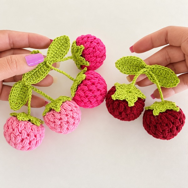 Hands holding crochet berry keyrings with green leaves